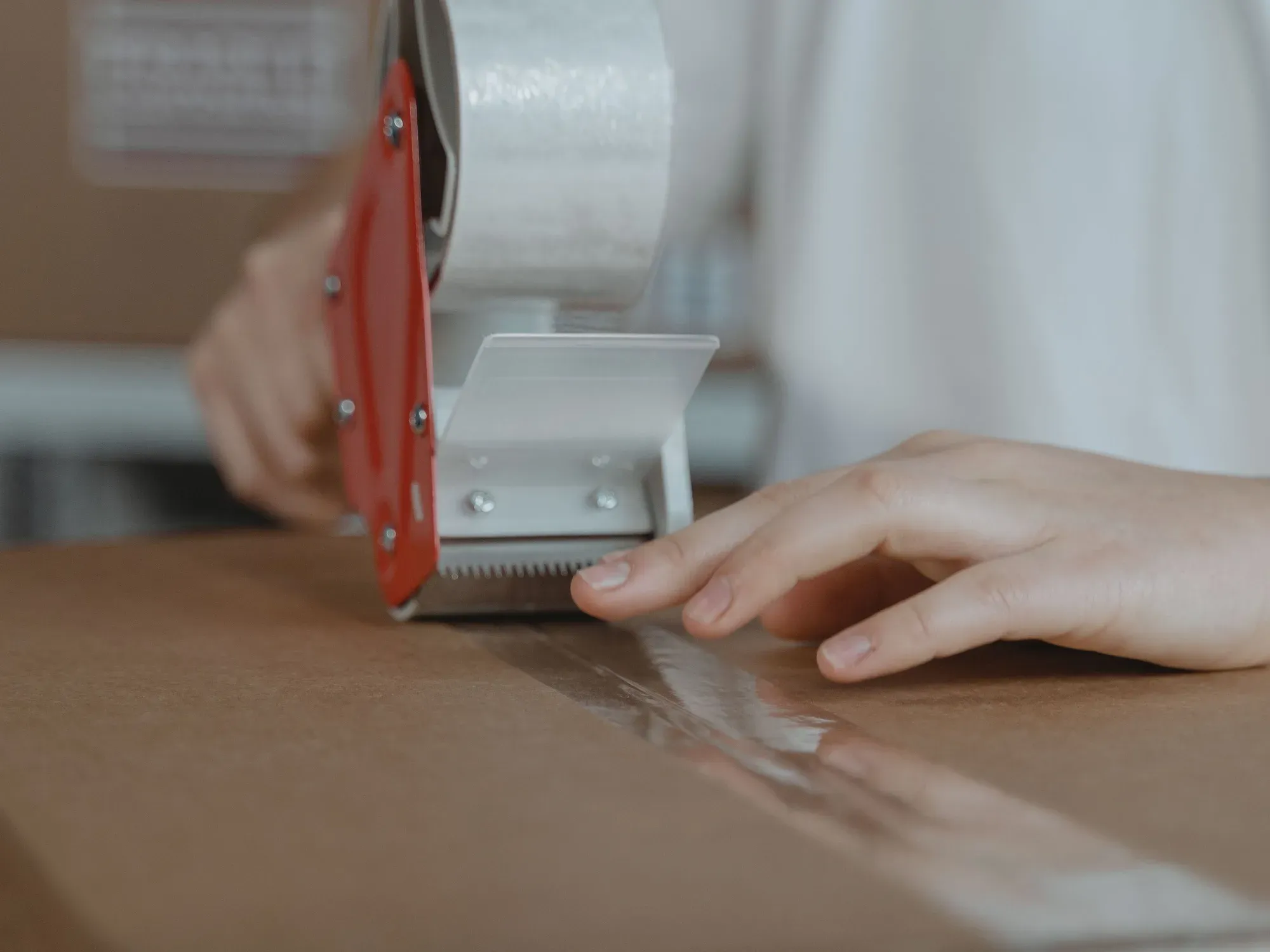 Karton wird am Packtisch mit einem Handabroller verklebt